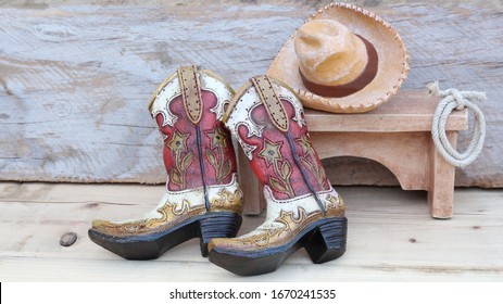 cowboy boots leaning on a bench with a hat and lasso sitting on a wood background with copy space