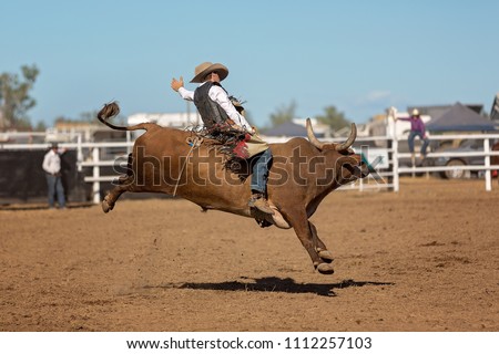 A cowboy competing in a bullriding event at a country rodeo