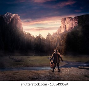 Cowboy holding a guitar in the nature surrounded by mountains and trees.