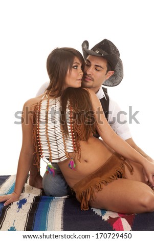 A cowboy and Indian couple are sitting together on a blanket about to kiss.