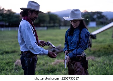 Cowboy Man Standing At The Green Land Near Mountain Side Teaching Cow Girl How To Handle Revolver Gun And Load Bullet To The Chamber Gun Piston 
