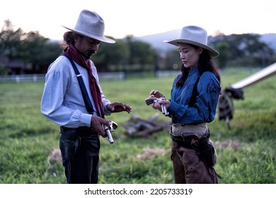 Cowboy Man Standing At The Green Land Near Mountain Side Teaching Cow Girl How To Handle Revolver Gun And Load Bullet To The Chamber Gun Piston 
