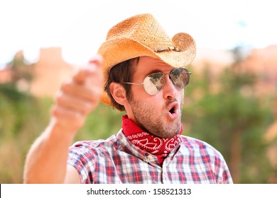 Cowboy man with sunglasses and cowboy hat pointing at camera saying WE WANT YOU. Male model in american rural western countryside landscape nature on ranch or farm, Utah, USA.