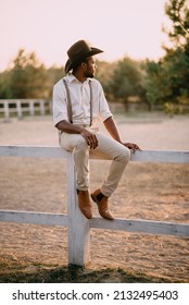 Cowboy on ranch. Young African American man sits on fence and looks into distance.