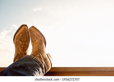 cowboy resting legs with feet crossed - sky background - negative space - boots