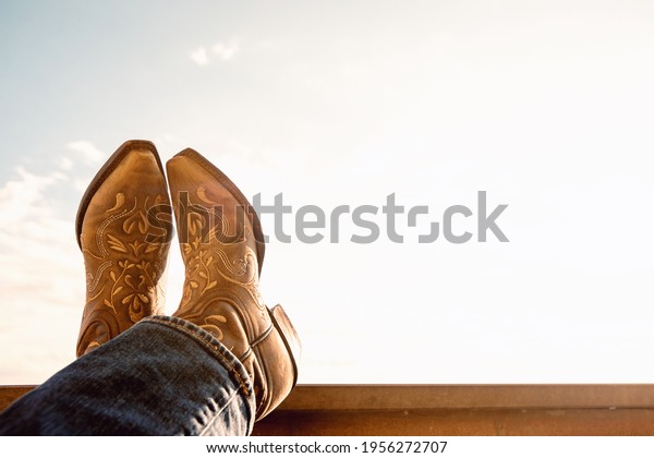 cowboy resting legs with feet crossed - sky\
background - negative space -\
boots