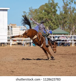 Cowboy riding a bucking bronco horse in a competition at a country rodeo