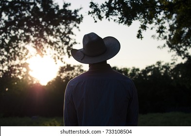 Cowboy silhouette against sunset on country ranch.  