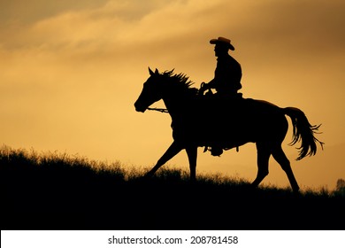 A cowboy silhouette riding on a mountain with an yellow sky.
