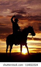 A cowboy is sitting on his horse in the sunset and swinging a rope.