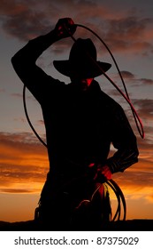 A cowboy is standing in the sunset with a rope.