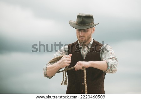 Cowboy wearing hat. Western life. Handsome bearded west farmer. Portrait of man cowboy or farmer. Western. Cowboy with lasso rope on sky background.