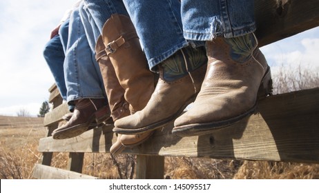 Cowboys and cowgirls sitting on wooden fence.