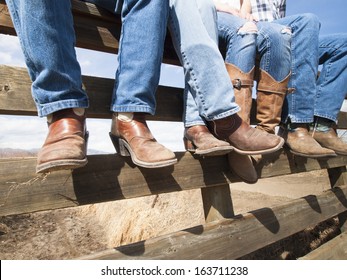 Cowboys And Cowgirls Sitting On Wooden Fence.