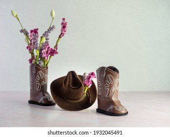 Cowgirl or cowboy brown hat with cowgirl or cowboy brown leather boots with one boot filled with pink and purple artificial flowers and more flowers adorning the hat, cute western fashion apparel.  