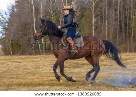 Cowgirl in a cowboy hat rides a horse on the background of the forest