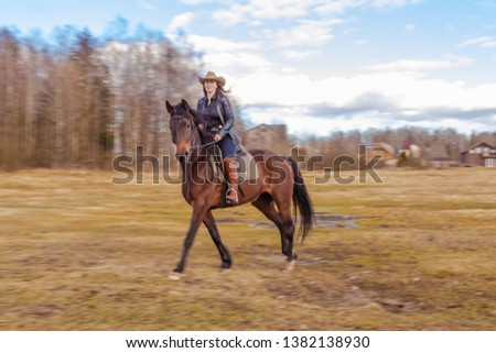 Cowgirl in a cowboy hat rides a horse on the background of the forest.
Motion blur effect.