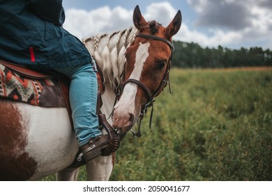 Cowgirl riding a horse in the rain. Western boot with spur. Horse head close up.