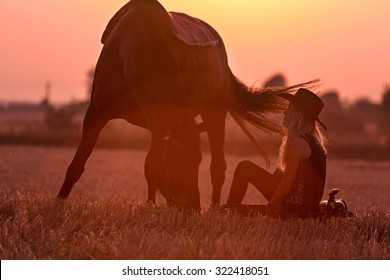 Cowgirl sitting near her grazing horse.
