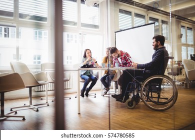 Coworker on wheelchair with photo editors in meeting room at creative office