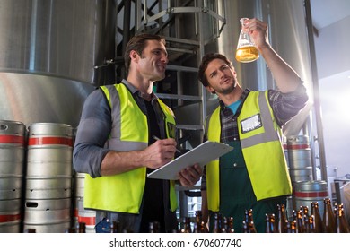 Coworkers examining beer in beaker at warehouse - Powered by Shutterstock