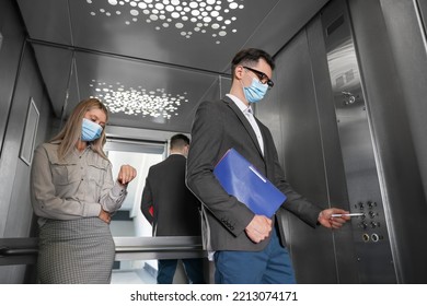 Coworkers With Face Masks In Elevator, Man Using Pen To Choose Floor, Low Angle View. Protective Measure