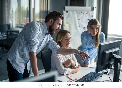 Coworkers Looking At A Computer And Talking About Work.