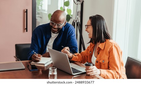 Co-workers in a modern office engaged in brainstorming and laughing together, portraying a casual and collaborative work environment. - Powered by Shutterstock