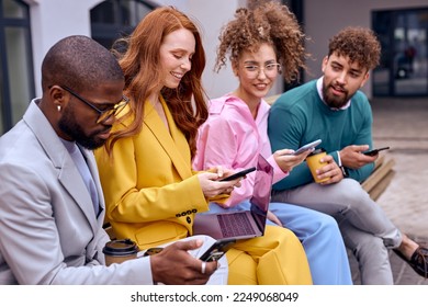 co-workers sit in row on bench using smartphone, dressed in stylish colourful formal clothes,caucasian men and women after meeting, have rest during break. leisure. focus on redhead lady