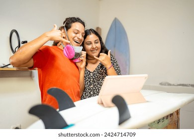 Coworkers of a surfboard repair shop in an online meeting with a digital tablet gesturing to be cool and fine - Powered by Shutterstock