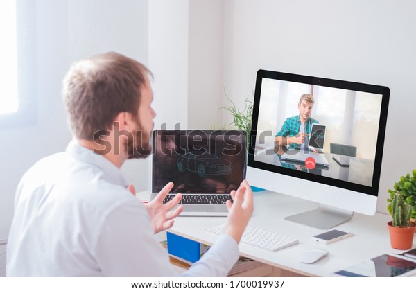 Coworkers in a virtual\
meeting from home. Young man in front of the computer screen\
talking on video\
conference