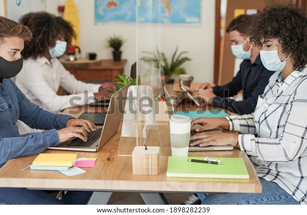 Coworking office with dividers and multiracial\
staff wearing protective face masks for coronavirus - Workplaces\
and safety measures
