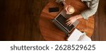 Co-working space, freelance and e-learning concept. Top view, male hands holding cup of coffee and using laptop. A man sitting in cafe and working or studying online.