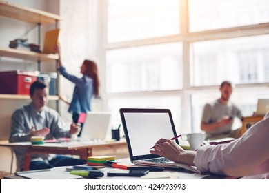 Coworking Station. Modern Business Loft And Millenials Working Together. Blank Laptop Typing. Intentional Sun Glare And Blurry Background