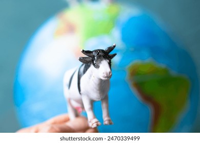Cows breeding and CO2 emission idea concept. Plastic toy cow in front of world model background. Cattle farming. Methane emissions from livestock. Animal. Horizontal photo. No people, nobody. 
