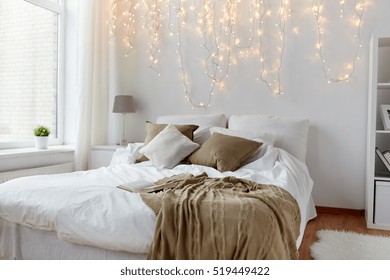 coziness, comfort, interior and holidays concept - cozy bedroom with bed and christmas garland lights at home - Powered by Shutterstock