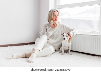 Сoncept of coziness, home comfort and leisure. Portrait of a stylish 40s woman dressed in a white cozy knitted sweater enjoying morning coffee, holding a mug - Powered by Shutterstock