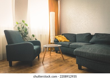 Cozy apartment living room with sofa and yellow pillows and stylish table with book by flower and window with blue light outside in winter. Grey armchair .copy paste wall background - Shutterstock ID 2208912935