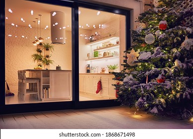 cozy apartment with sliding doors, and decorated christmas tree on the patio at snowy winter night
