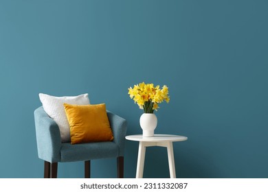 Cozy armchair with cushions and blooming narcissus flowers on coffee table near blue wall - Shutterstock ID 2311332087