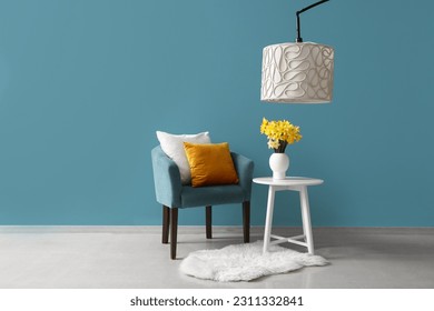 Cozy armchair with cushions and blooming narcissus flowers on coffee table near blue wall - Shutterstock ID 2311332841