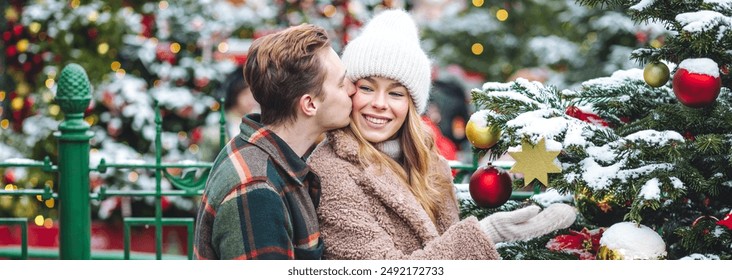 Cozy atmosphere of outdoor christmas market. Festive mood, holiday spirit. Young beautiful loving couple drinking homemade hot tea or mulled wine from terms bottle. Enjoying winter vacations banner - Powered by Shutterstock