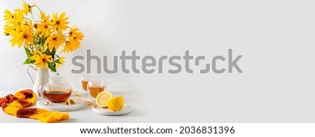 Cozy autumn banner. Hot teapot, two cups of tea, yellow flowers bouquet, lemon and knitted scarf on white background side view. Autumn, fall, tea party concept. Restaurant Web line, sale. Copy space 