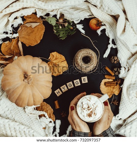 Cozy Autumn Composition. Woman Hands with Pumpkin Latte, Cinnamon, plaid on a Black Background
