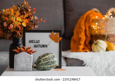 Cozy autumn concept. Home warmth in cold weather. Still-life. A blanket, pumpkins, flowers and the inscription home on the coffee table in the home interior of the living room. - Shutterstock ID 2191198417