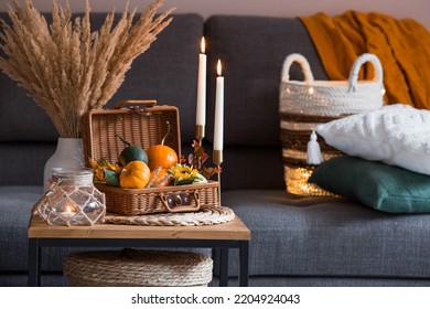 Cozy autumn concept. Home warmth in cold weather. Still-life. Pumpkins, wicker basket, candles and flowers on the coffee table in the home interior of the living room. - Shutterstock ID 2204924043