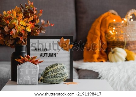 Cozy autumn concept. Home warmth in cold weather. Still-life. A blanket, pumpkins, flowers and the inscription home on the coffee table in the home interior of the living room.