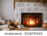 Cozy autumn. Cup of tea, pumpkin, autumn leaves on wooden table on background of warm fireplace. Fall still life in living room. Thanksgiving and Halloween.