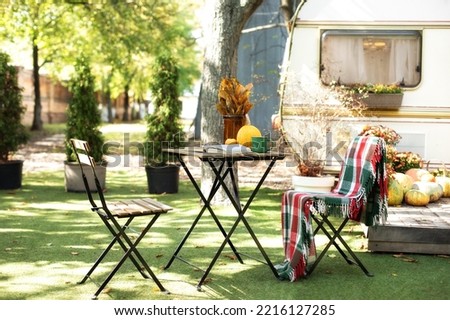 Cozy autumn garden with chair and table decorated for Halloween. Backyard with orange pumpkin. Furniture in fall garden for Picnic or leisure in nature. Leaves in vase, books and cup with tea on table