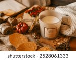 Cozy autumn scene with a vanilla caramel latte scented candle surrounded by warm autumn decor, including dried leaves, a knitted blanket, and seasonal elements.